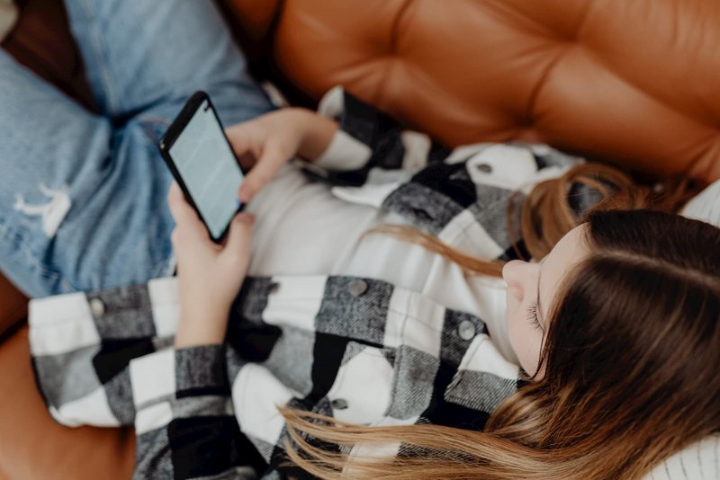Mädchen liegt auf Sofa und surft mit Mobiltelefon im Internet